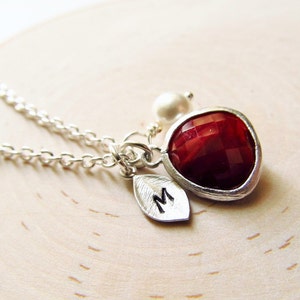 Peut inclure: Un collier en argent avec un pendentif en forme de cœur rouge, un petit pendentif en perle et un pendentif en forme de feuille gravé de la lettre "M".