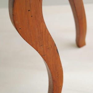 K&ouml;nnte beinhalten: Nahaufnahme eines gebogenen Holzm&ouml;belfu&szlig;es. Das Bein hat eine warme braune Farbe mit sichtbarer Holzmaserung und kleinen dunklen Flecken. Das Design ist elegant und klassisch, was auf ein Vintage- oder antikes St&uuml;ck hindeutet.