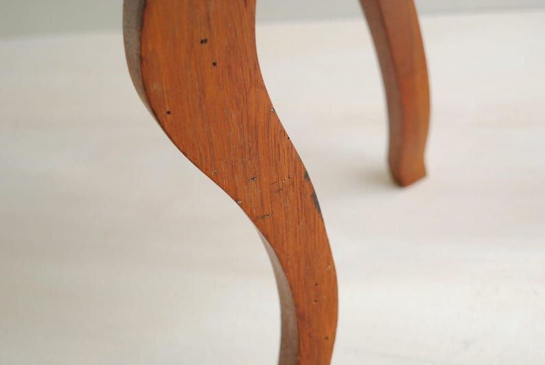 K&ouml;nnte beinhalten: Nahaufnahme eines gebogenen Holzm&ouml;belfu&szlig;es. Das Bein hat eine warme braune Farbe mit sichtbarer Holzmaserung und kleinen dunklen Flecken. Das Design ist elegant und klassisch, was auf ein Vintage- oder antikes St&uuml;ck hindeutet.