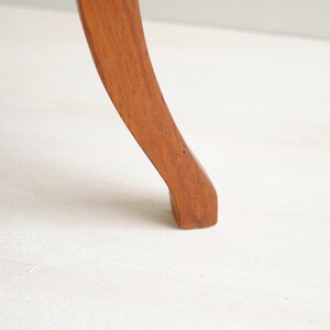 K&ouml;nnte beinhalten: Ein gebogenes Holzm&ouml;belbein, wahrscheinlich von einem Stuhl oder Tisch, wird vor einem wei&szlig;en Hintergrund dargestellt. Das Bein hat eine warme, mittelbraune Farbe mit einer glatten, polierten Oberfl&auml;che. Das Design ist klassisch und elegant.