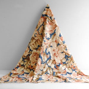 May include: A piece of fabric featuring a large-scale floral pattern with cream and peach-colored blossoms and leaves set against a deep navy blue background. The textile is draped in a triangular shape, showcasing the intricate botanical print.