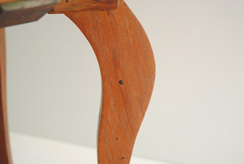 K&ouml;nnte beinhalten: Nahaufnahme eines h&ouml;lzernen Tischbeins mit geschwungenem Design. Das Bein besteht aus hellbraunem Holz und hat eine glatte, polierte Oberfl&auml;che. Das Bein ist an einer Tischplatte aus Holz befestigt. Der Hintergrund ist eine schlichte wei&szlig;e Wand.