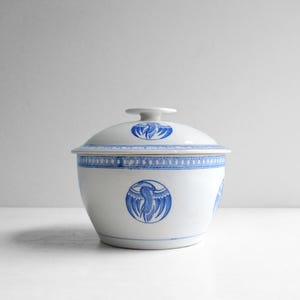 Puede incluir: Cuenco de cerámica blanco con tapa, con diseños de pájaros azules. El cuenco tiene forma redondeada con tapa y un pequeño asa. El diseño del pájaro se repite alrededor del cuenco y en la tapa.
