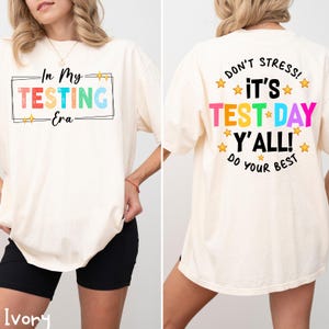 May include: Ivory t-shirt with a rainbow graphic that says "In My Testing Era" on the front and "Don't Stress! It's Test Day Y'all! Do Your Best" on the back.