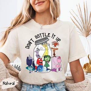 Peut inclure: Un t-shirt blanc avec un graphique des personnages du film Vice-Versa dans un bocal en verre. Le texte "Ne pas mettre en bouteille" est imprimé au-dessus du bocal.