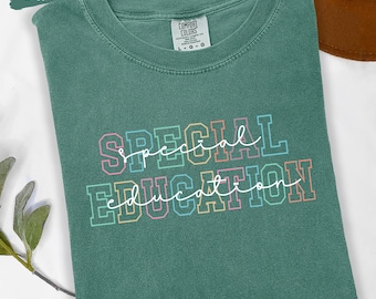 May include: A light green t-shirt with the words "SPECIAL EDUCATION" in a colorful, outlined font. The shirt is folded and has a tag that reads "COMFORT COLORS". The words are in a mix of script and block letters.