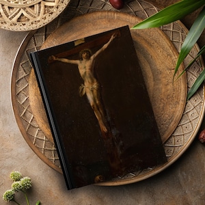 May include: A black hardcover journal with a painting of a person on a cross. The painting is in a dark, muted color palette.