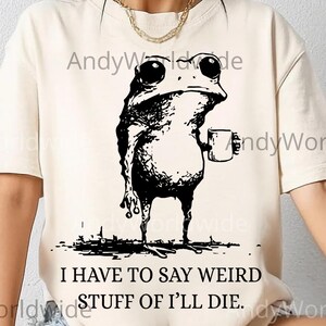 Puede incluir: Camiseta color crema con una ilustración negra de una rana sosteniendo una taza. El texto "I HAVE TO SAY WEIRD STUFF OF I'LL DIE" está debajo de la rana. La parte inferior de la imagen tiene el texto "DIGITAL DOWNLOADS PNG".