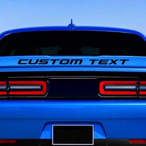 May include: A blue Dodge Challenger with black custom text on the rear window. The text reads "CUSTOM TEXT".