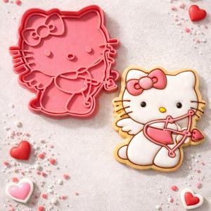Può includere: Un tagliabiscotti rosa di Hello Kitty e un biscotto decorato con fiocco, ali e arco e freccia. Zuccherini e caramelle a forma di cuore rossi e rosa sono sparsi intorno ai biscotti su una superficie bianca.