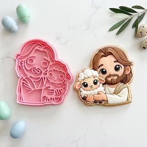 May include: A pink plastic cookie cutter and a decorated cookie featuring a cartoon depiction of a person holding a lamb. The cookie has brown hair and a beard. Pastel-colored Easter eggs are scattered around the image.