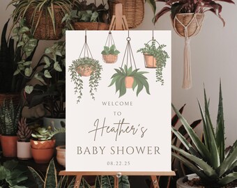 May include: A white welcome sign with a green and brown illustration of hanging plants. The sign reads "Welcome to Heather's Baby Shower 08.22.25".