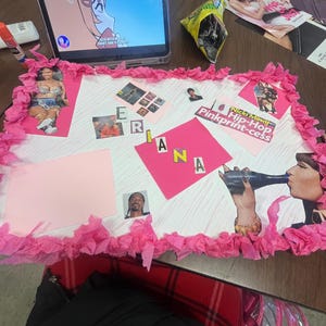 May include: A pink and white poster board with the word "Rihanna" spelled out in pink letters. The poster board is decorated with pictures of Rihanna, Nicki Minaj, and Snoop Dogg. The text "Nicki Minaj Hip-Hop Pinkprint-cess" is written on the poster board.