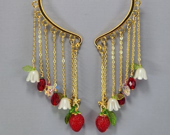 Könnte beinhalten: Goldener Ohrclip mit herabhängenden Ketten und Anhängern. Die Anhänger bestehen aus roten und weißen Blumen, roten Beeren und grünen Blättern.