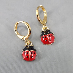 May include: A pair of gold hoop earrings with a red and black ladybug charm hanging from each hoop.