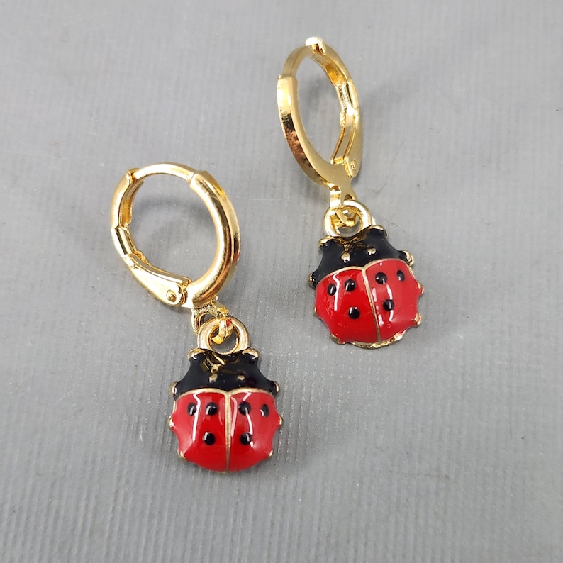 May include: A pair of gold hoop earrings with a red and black ladybug charm hanging from each hoop.