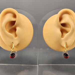 May include: A pair of gold hoop earrings with a dangling ladybug charm. The ladybug is red with black spots and black accents.
