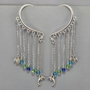 May include: Silver ear cuffs with dangling chains, blue and green beads, and dolphin and turtle charms. The ear cuffs curve around the ear and are connected by a silver bar.