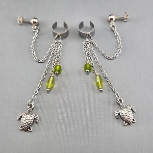 Könnte beinhalten: Ein Paar silberne Ohrclips mit baumelnden Ketten und grünen Glasperlen. Jede Kette endet mit einem silbernen Schildkrötenanhänger.