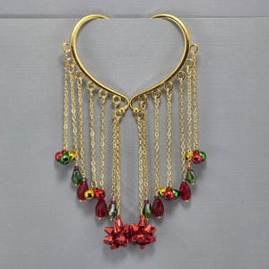 Può includere: Polisini per orecchie dorati con catenine pendenti, fiocchi rossi e perline colorate. Le catenine sono decorate con perline rosse, verdi e dorate e campanellini. Un accessorio unico e festoso.