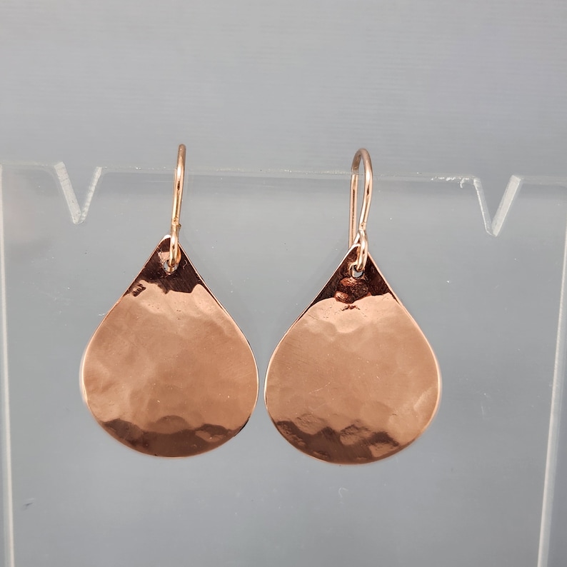May include: A pair of rose gold teardrop earrings with a hammered texture.
