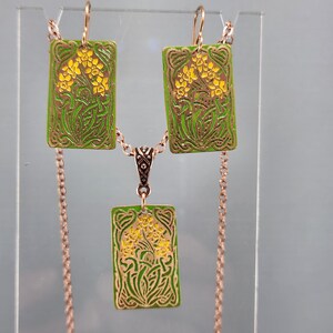 May include: A set of gold-tone earrings and a necklace with green and yellow enamel floral designs. The earrings and pendant are rectangular in shape.