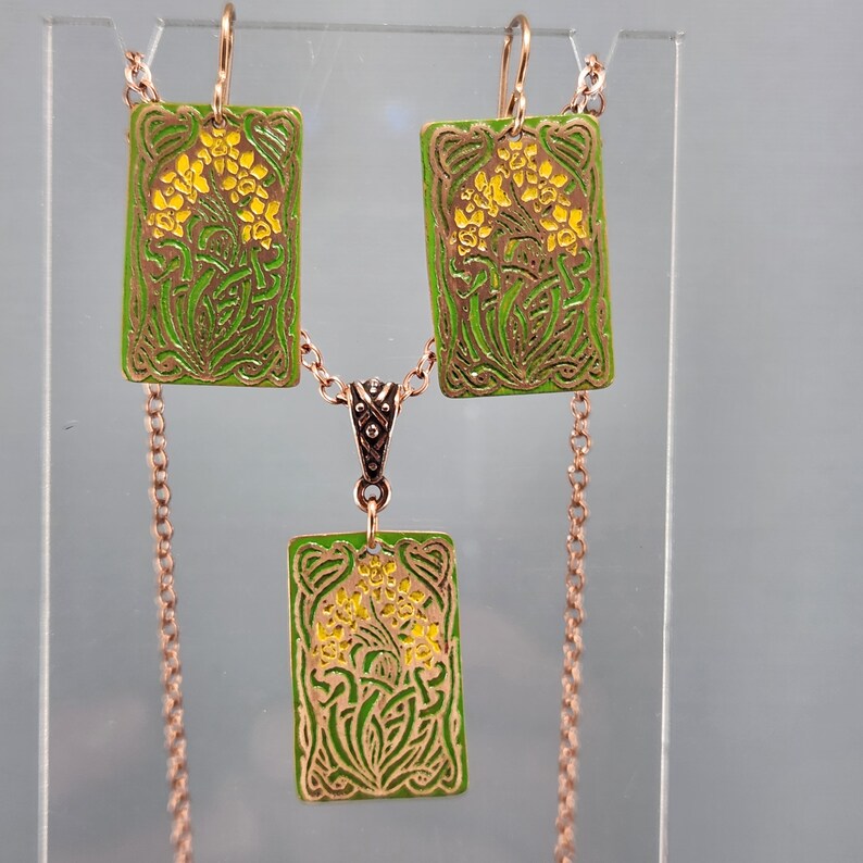 May include: A set of gold-tone earrings and a necklace with green and yellow enamel floral designs. The earrings and pendant are rectangular in shape.