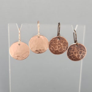 May include: Three pairs of hammered copper earrings. The earrings are round and have a textured surface. The earrings are on a white display stand.