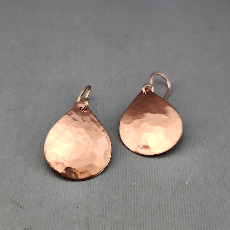 May include: A pair of hammered copper teardrop earrings with a shiny finish.