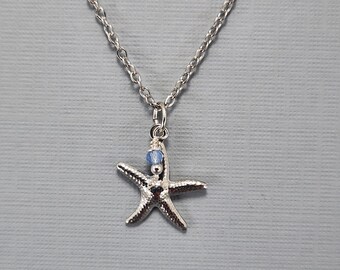 May include: A silver necklace featuring a starfish pendant and a blue crystal bead. The chain is a delicate silver chain.