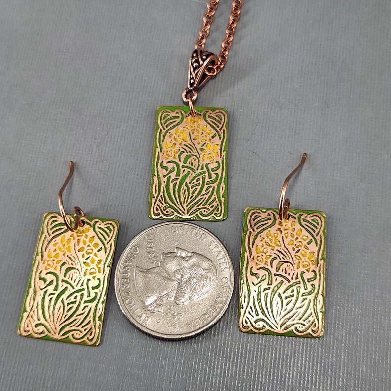 May include: A set of copper jewelry with a green and yellow enamel design. The set includes a necklace and a pair of earrings. The design features a stylized floral motif.