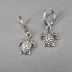 May include: A pair of silver hoop earrings with a silver turtle charm hanging from each hoop.