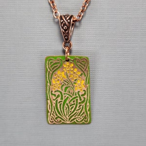 May include: A copper pendant necklace with a green and yellow enamel design of stylized flowers. The pendant is rectangular and has a Celtic knot border.