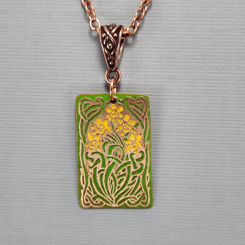 May include: A copper pendant necklace with a green and yellow enamel design of stylized flowers. The pendant is rectangular and has a Celtic knot border.