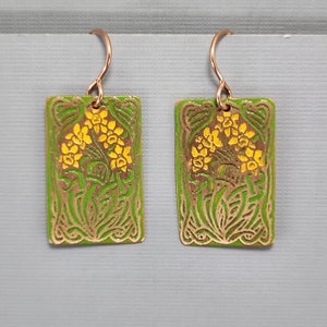 May include: A pair of green and gold earrings with a floral design. The earrings are rectangular and have a hook closure.