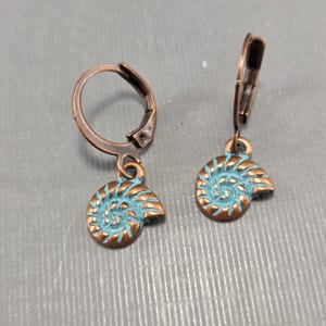 May include: A pair of bronze-colored leverback earrings with a spiral nautilus shell design. The shell details are painted in a turquoise blue color, creating a contrast with the bronze metal. The earrings are designed for pierced ears.