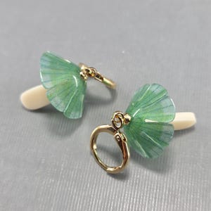 May include: A pair of green ginkgo leaf earrings with gold-toned hoops. The leaves have a translucent, almost iridescent quality.