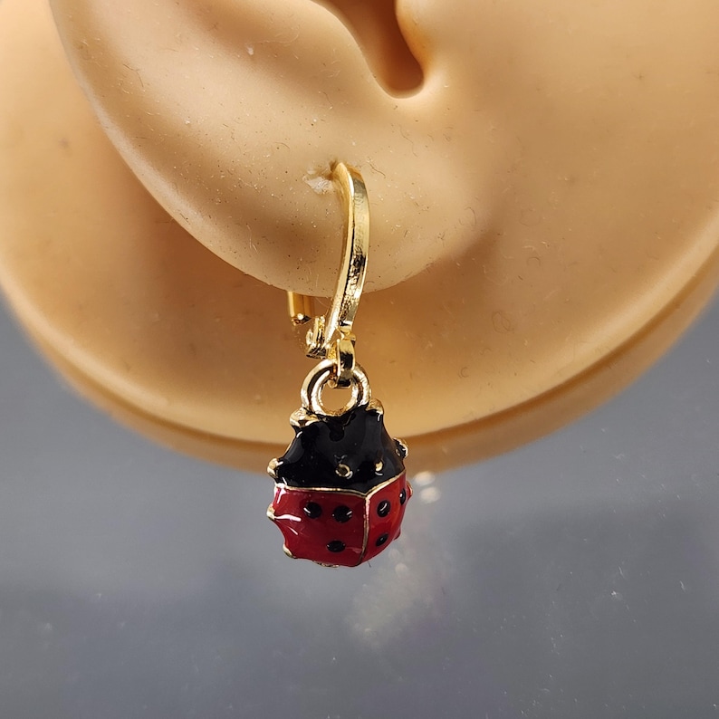 May include: Gold hoop earrings with a dangling ladybug charm. The ladybug is red with black spots and a black head.