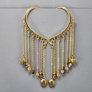 May include: A pair of gold-toned ear cuffs featuring a curved frame with multiple dangling chains. Each chain is adorned with small metallic sea turtle charms, iridescent shell beads, and smooth teardrop-shaped beads in a warm golden hue.