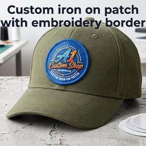 May include: An olive green baseball cap featuring a circular blue iron-on patch with an embroidery border. The patch displays the text A1 Custom Shop The Patch Lab Custom Iron-On Patch. Three additional white circular patches are placed nearby.