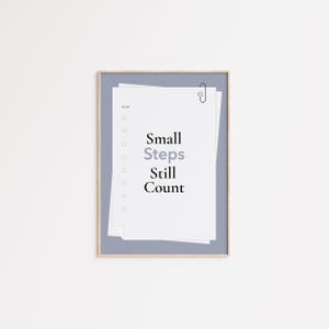 Può includere: Stampa incorniciata con una pila di carta bianca e un bordo blu. Il testo "Small Steps Still Count" è stampato in nero e grigio. Una graffetta argentata tiene insieme i fogli.