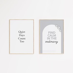 Può includere: Due stampe artistiche incorniciate con citazioni motivazionali. La stampa a sinistra recita "Quiet Days Count Too" in testo nero. La stampa a destra dice "Find Calm in the ordinary" con un design floreale in una combinazione di colori grigio e bianco.