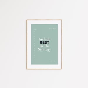 May include: A framed print with a light green background and the text "Include REST In The Strategy" in black and white. The words "DAILY PLAN" are at the top, and the author's name is at the bottom. The frame is a light brown color.