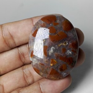 May include: An oval-shaped gemstone with a mix of translucent and opaque sections. The stone features a clear base with reddish-brown, irregularly shaped inclusions. The polished surface reflects light, highlighting the stone's natural patterns and textures.