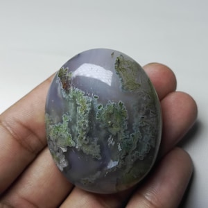 May include: A smooth, oval-shaped agate stone with a light purple base and green moss-like inclusions.