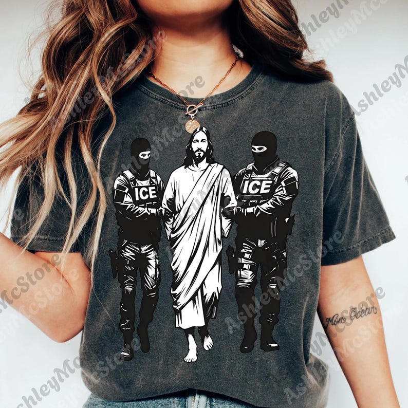 K&ouml;nnte beinhalten: Dunkelgraues T-Shirt mit einer Grafik von Jesus, flankiert von zwei Figuren in taktischer Ausr&uuml;stung, jeweils mit "ICE" auf ihren Westen. Die zentrale Figur ist wei&szlig;, im Kontrast zu den schwarzen Figuren.