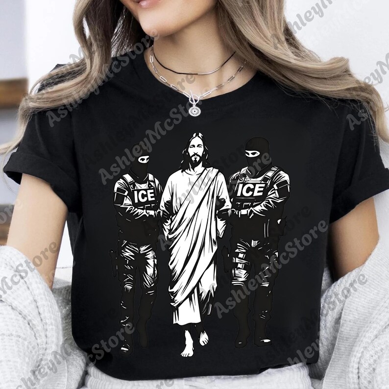 K&ouml;nnte beinhalten: Schwarzes T-Shirt mit einer wei&szlig;en Grafik, die Jesus zwischen zwei Figuren in taktischer Ausr&uuml;stung zeigt, jede mit "ICE" auf ihrer Uniform. Ein auff&auml;lliges, grafisches Design.