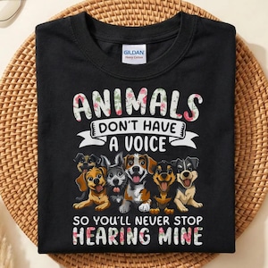 以下が含まれることがあります： 「ANIMALS DON'T HAVE A VOICE SO YOU'LL NEVER STOP HEARING MINE」の文字が花柄でデザインされた黒いTシャツ。6種類の犬種が描かれたグラフィックが特徴です。