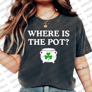 May include: Dark gray t-shirt with the text "WHERE IS THE POT?" in white. A white pot with a green shamrock is below the text. The shirt is a casual style.