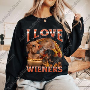 May include: Black sweatshirt with the text "I LOVE WIENERS" in orange. The graphic features several dachshunds and a hot dog. The design is centered on the front of the sweatshirt.